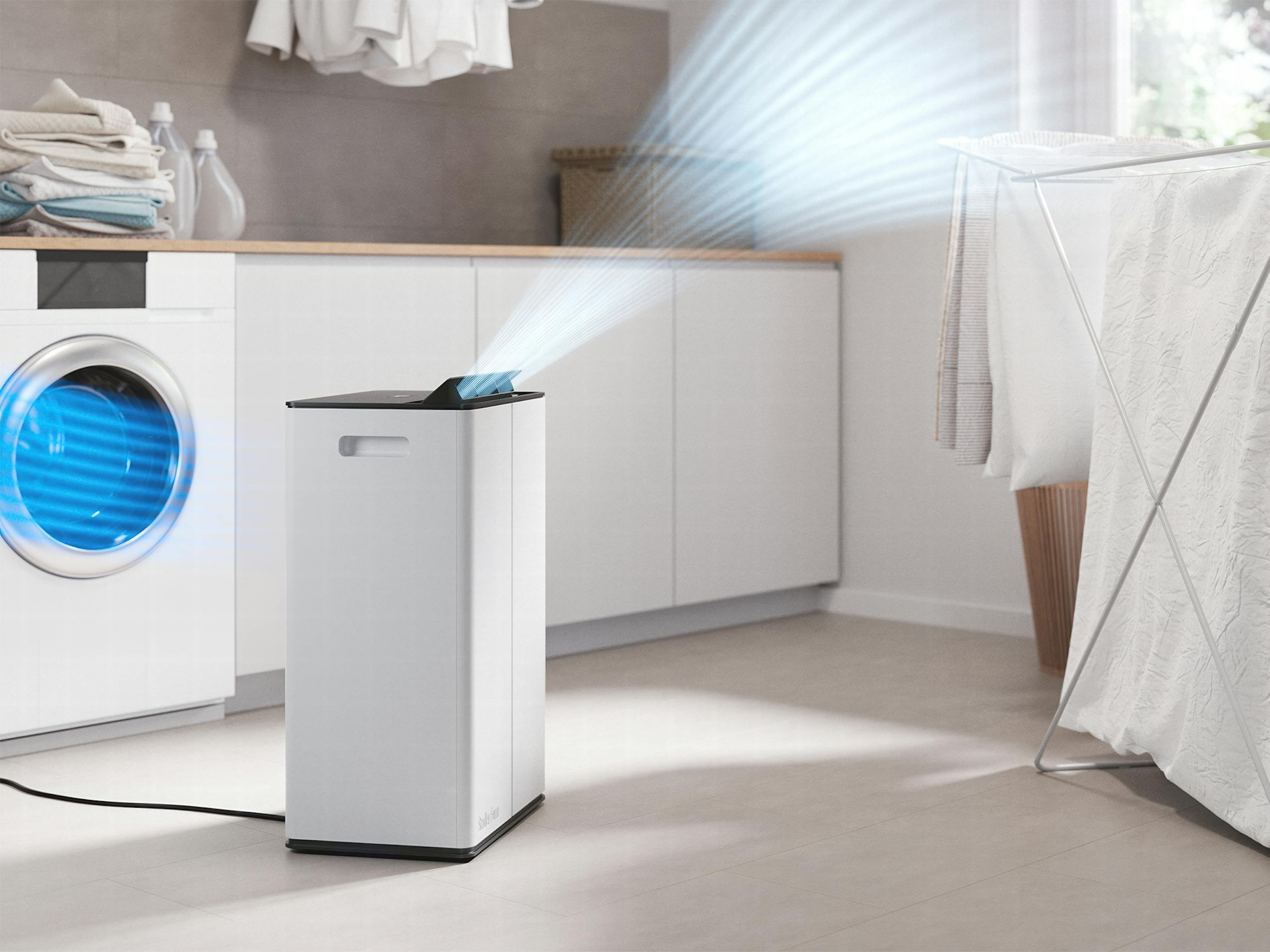 Purificatore d'aria bianco che emette aria blu. Lavanderia con lavatrice, stendibiancheria e bucato.