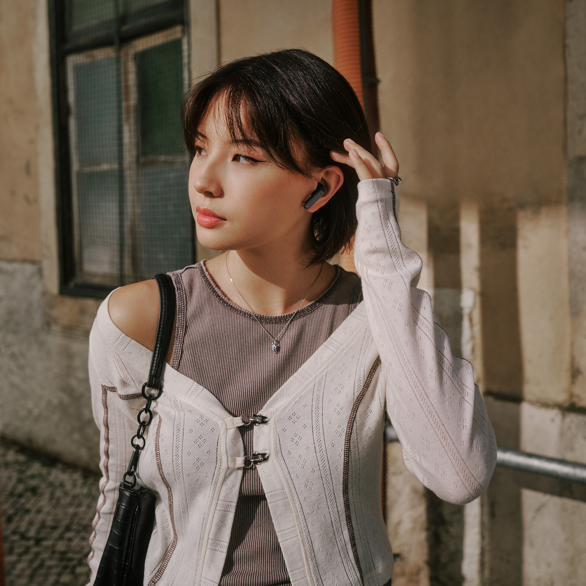 Femme avec un écouteur dans l'oreille, regardant ailleurs. Portant un cardigan blanc et un collier. Flou.