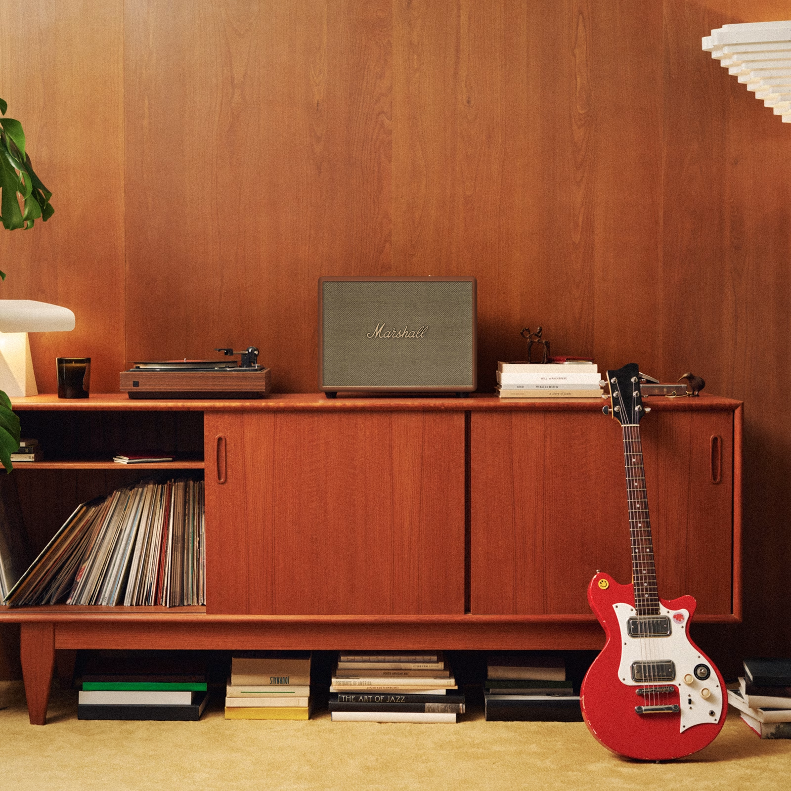 Altoparlante Marshall marrone su una credenza con dischi e una chitarra. Lo sfondo è una parete di legno.