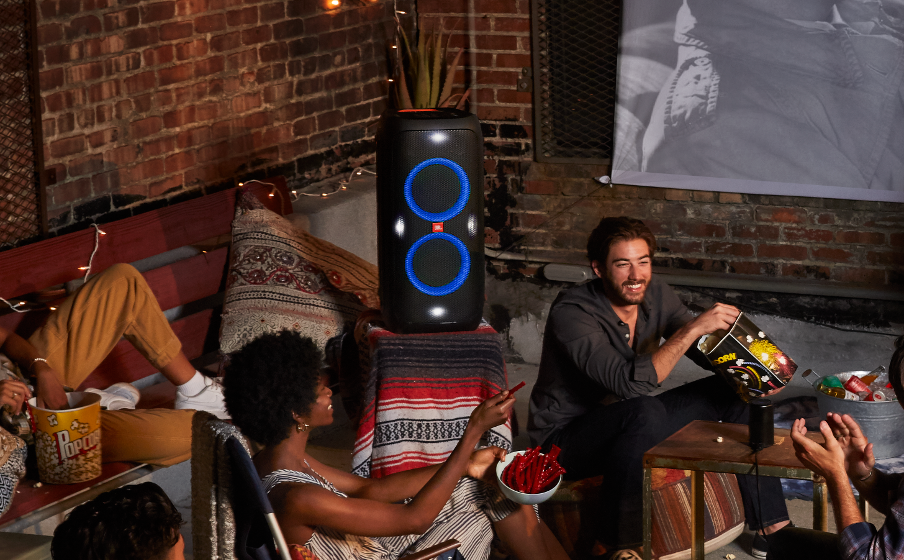 Leute bei einer Party im Freien mit Lautsprecher, essen Snacks und schauen einen Film.