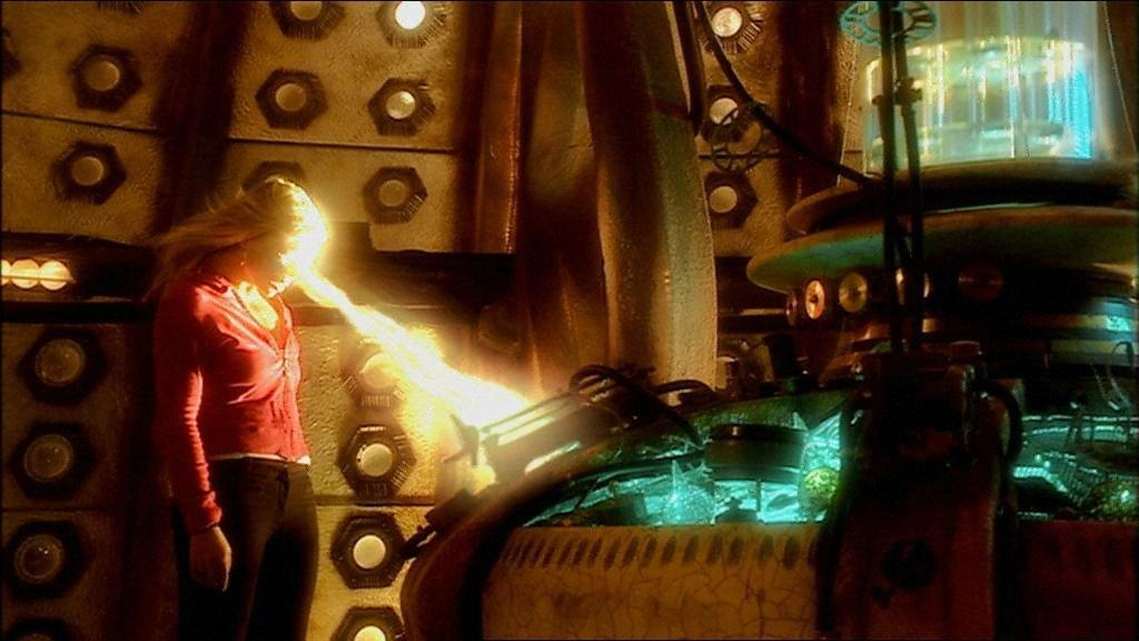 Eine Frau in roter Jacke wird von Licht getroffen, mit einer Maschine im Hintergrund. Der Raum hat ein futuristisches Design.