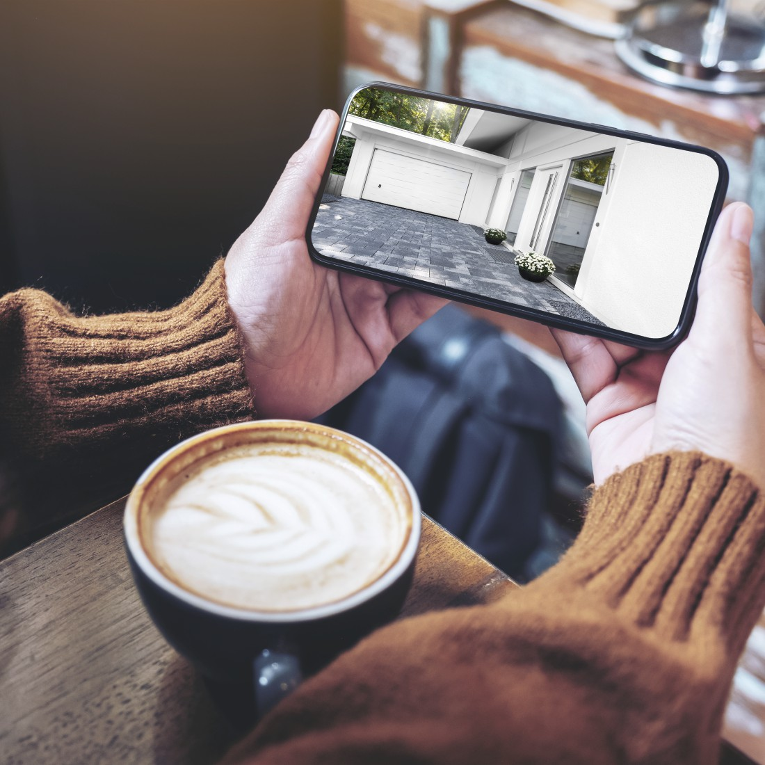 Person hält ein Telefon mit Garage. Kaffeetasse davor.