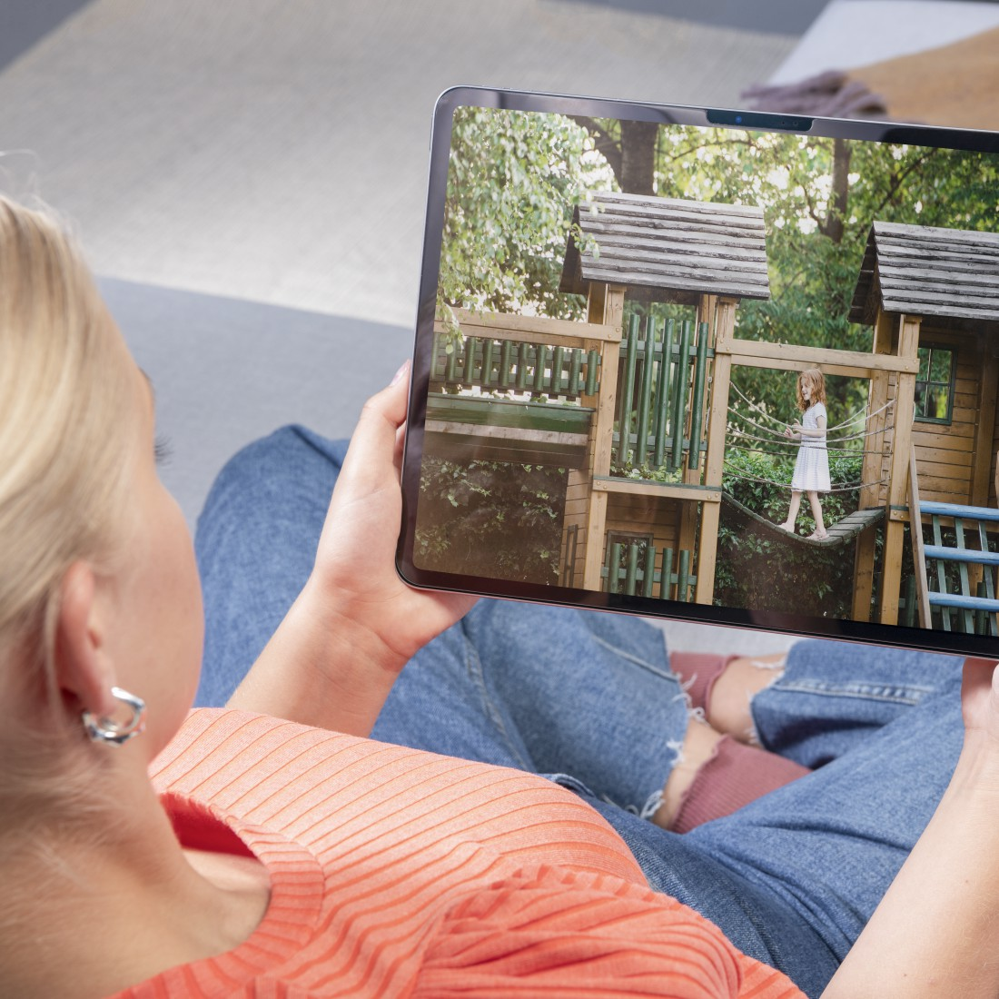 Frau hält Tablet mit Mädchen auf Holzbrücke in Spielplatz.
