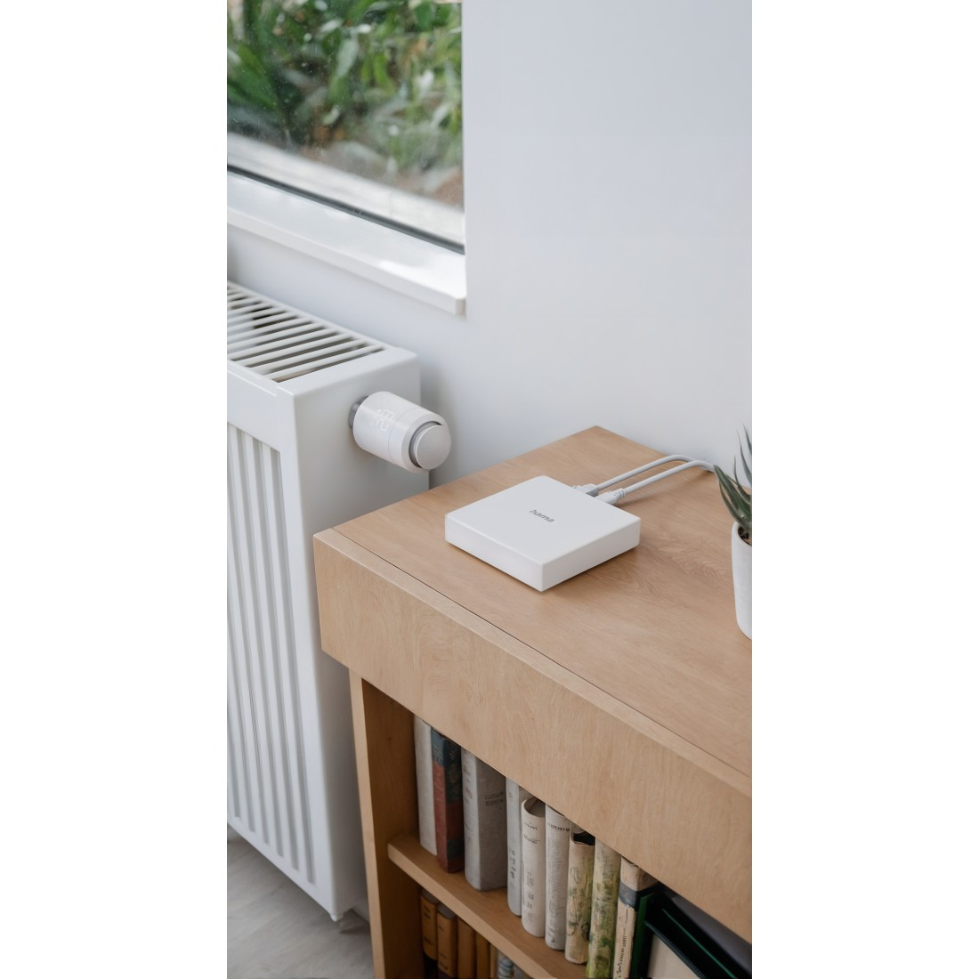 Weißes Smart-Home-Gerät auf einem Holztisch, in der Nähe eines Heizkörpers. Ein Thermostat ist sichtbar.