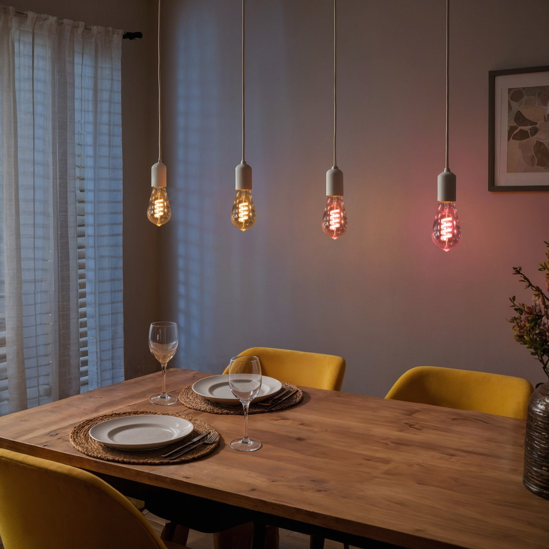 Esszimmer mit vier hängenden Glühbirnen, zwei Tellern und Gläsern auf dem Holztisch.