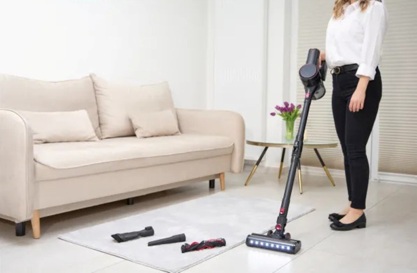 Kobieta trzymająca odkurzacz z akcesoriami na dywanie w pobliżu.