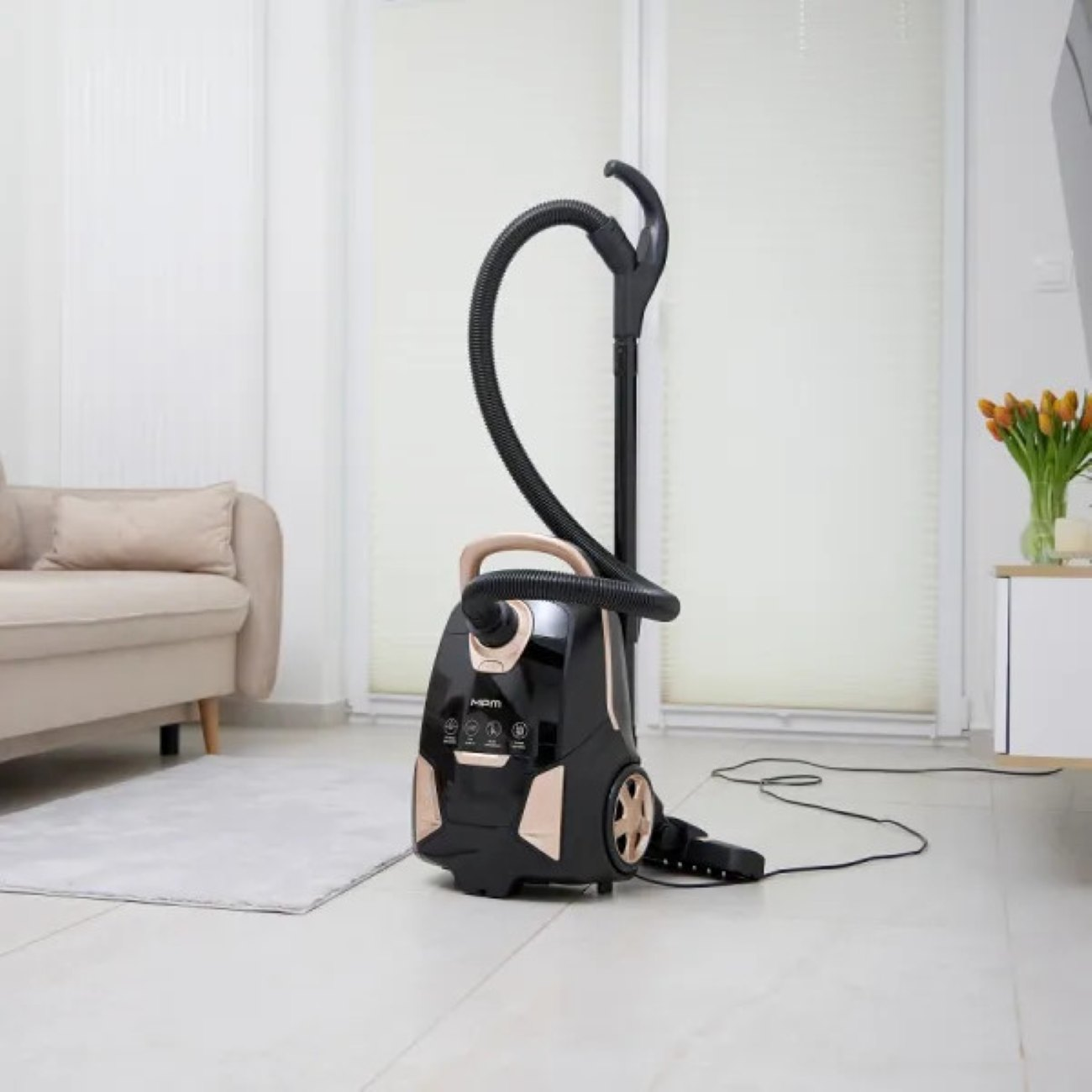 Czarny odkurzacz w pokoju z białymi ścianami, sofą i dywanem.