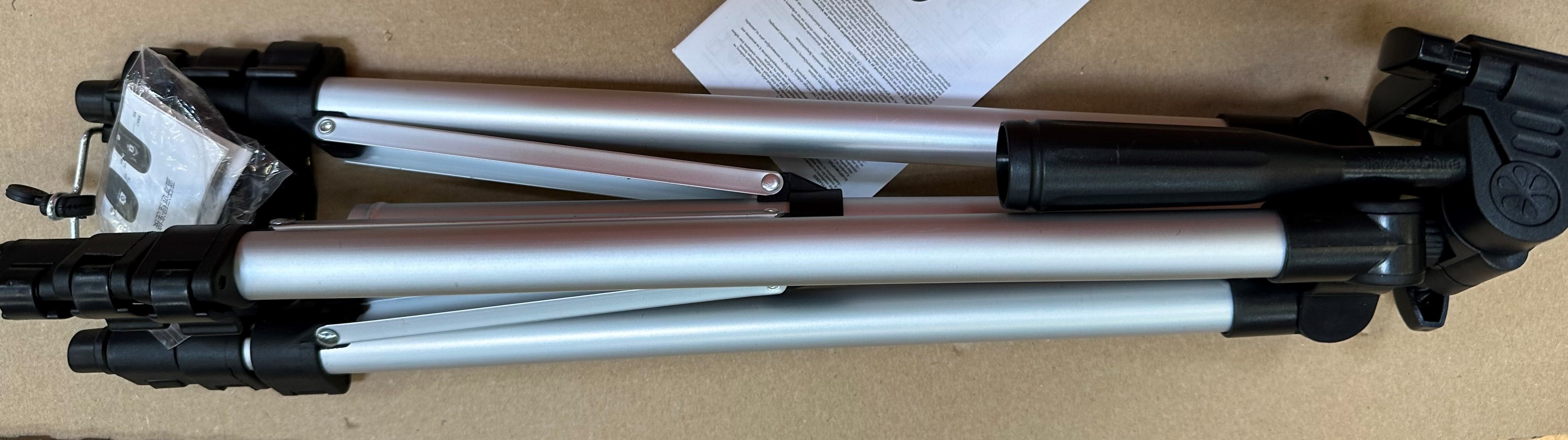 Złożony srebrny statyw z czarnymi detalami, leżący na kartonie, widok z góry.