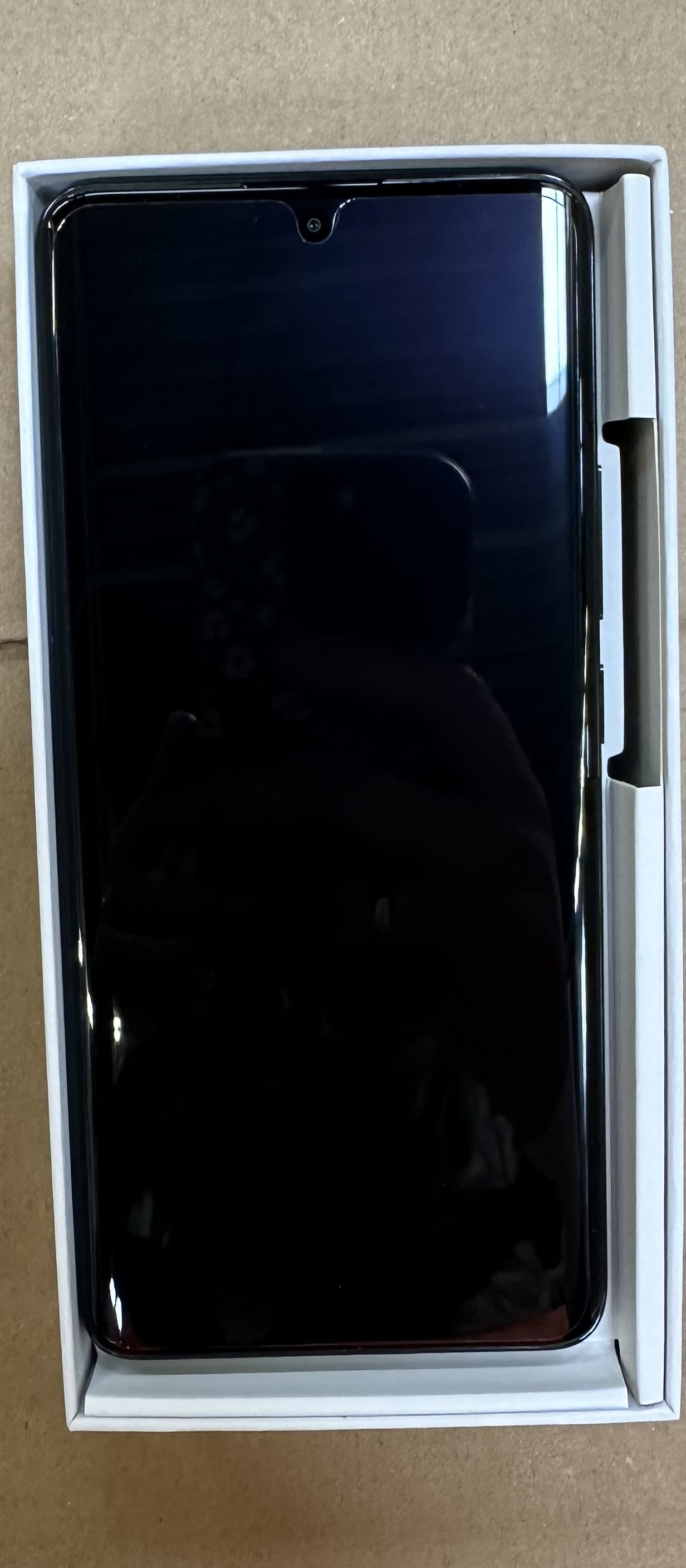 Czarny smartfon w białym pudełku. Widoczny ekran, z przednim aparatem u góry.