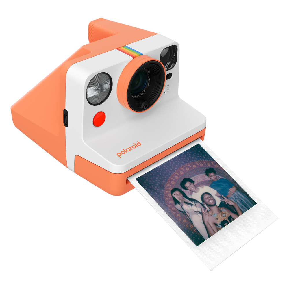 Turuncu ve beyaz Polaroid kamera, bir fotoğraf basıyor, beyaz bir yüzeyde.