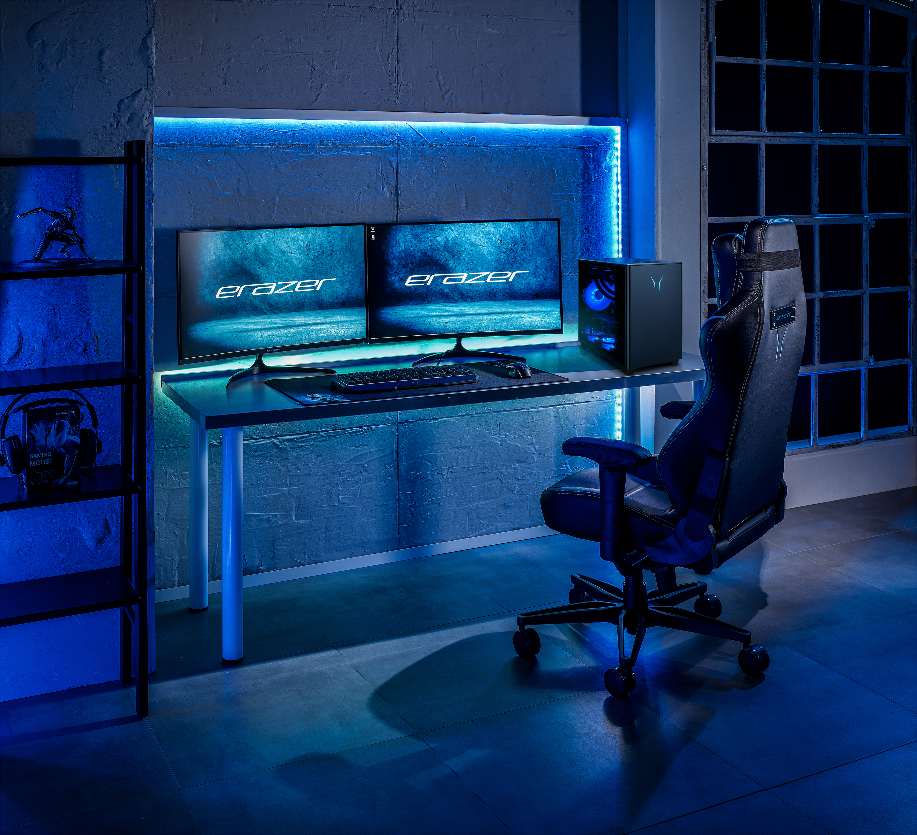 Gaming-Setup mit zwei Monitoren mit 'Erazer', Schreibtisch, Stuhl, PC und Regalen mit einer Figur.