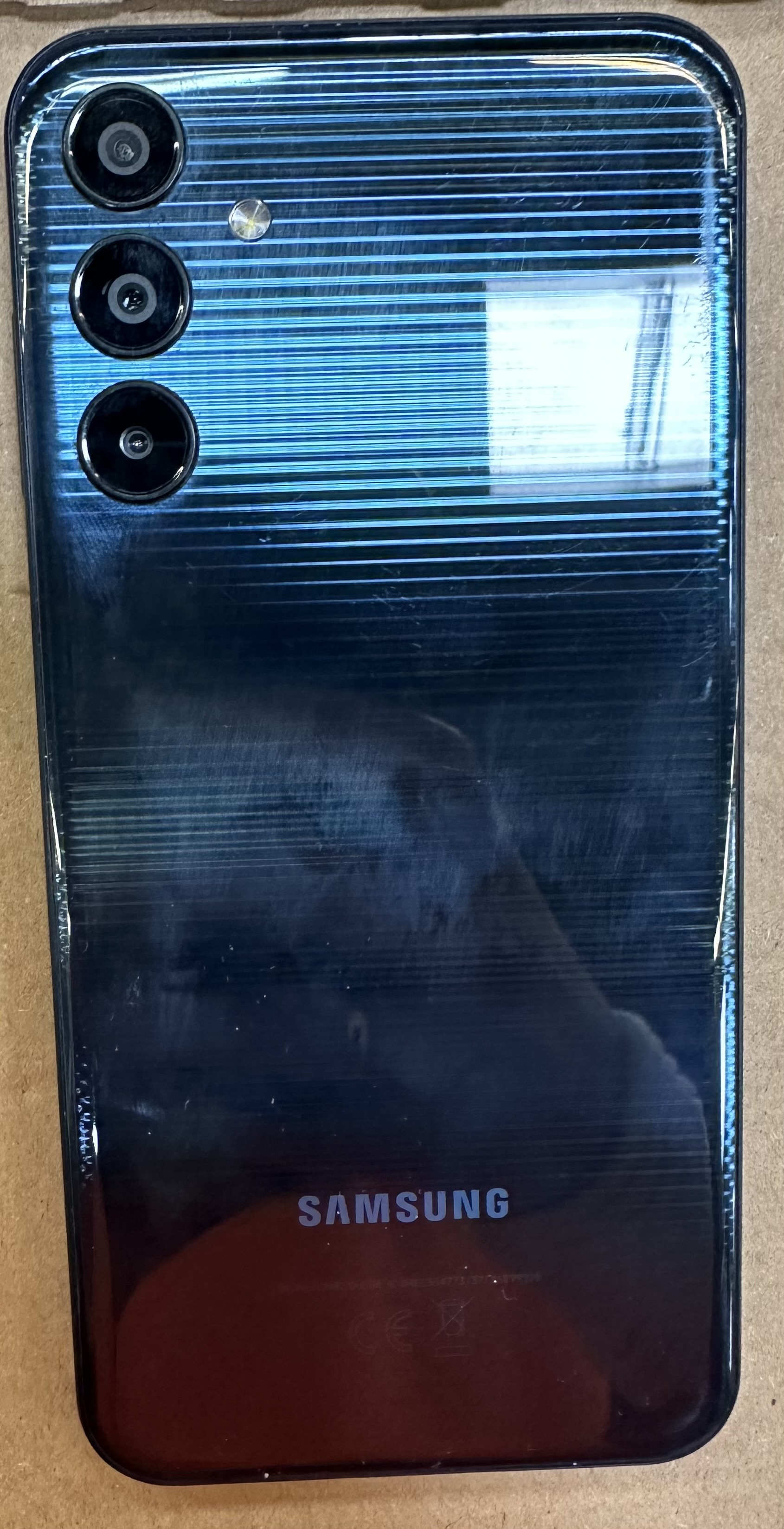 Czarny tył telefonu Samsung. Ma trzy obiektywy aparatu i lampę błyskową. Powierzchnia ma rysy i poziome linie.