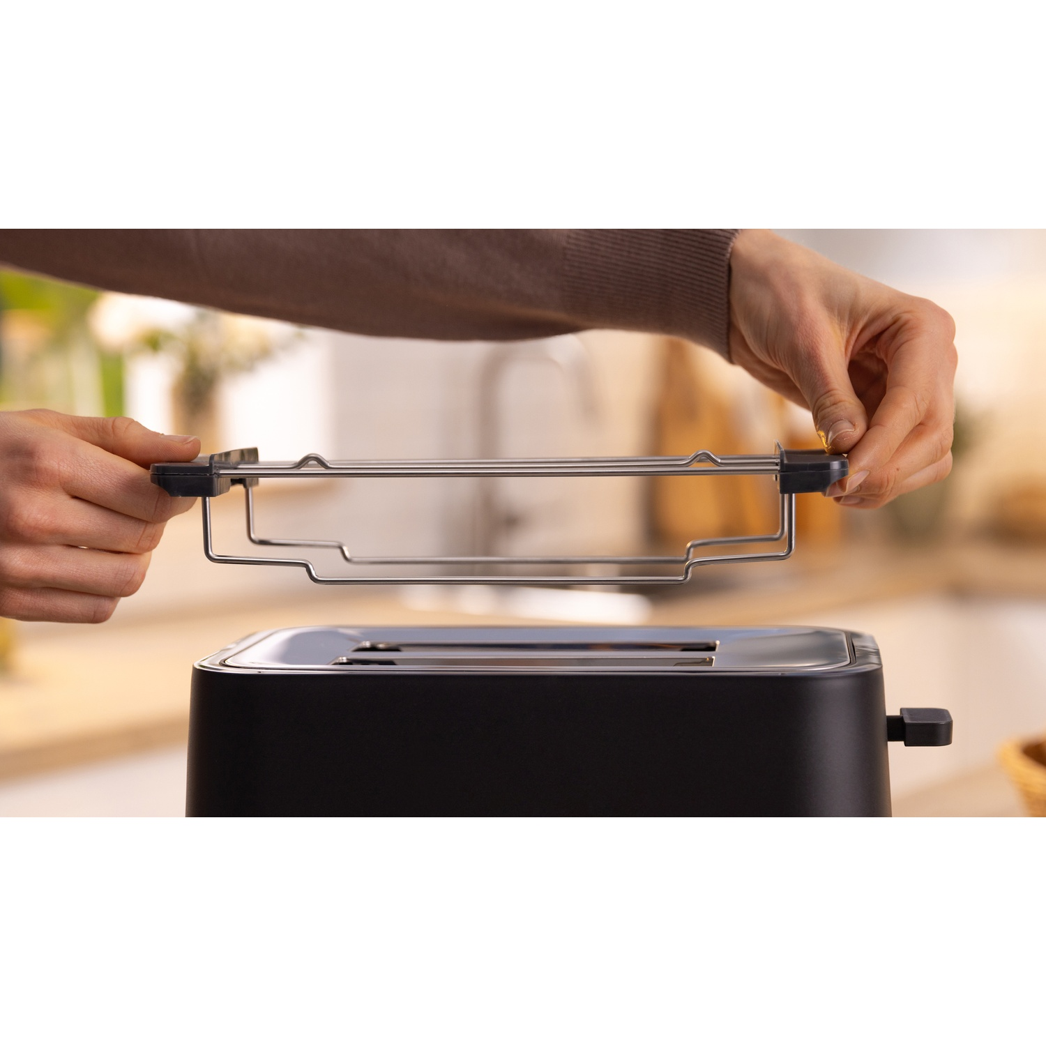 Mani che inseriscono una griglia all'interno di un tostapane nero. La griglia serve per tostare il pane.