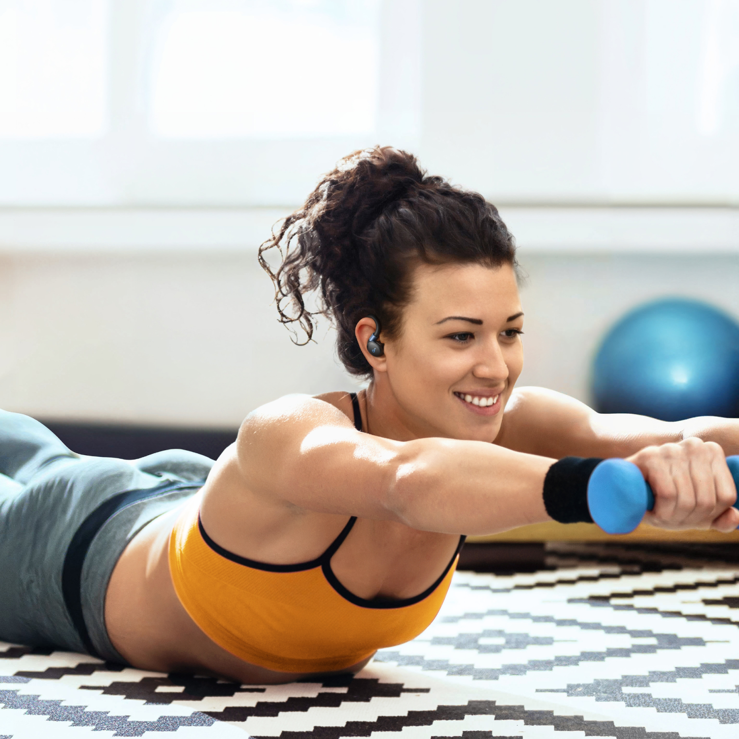 Vrouw die oefent met oortjes, dumbbells vasthoudt, draagt een oranje top.