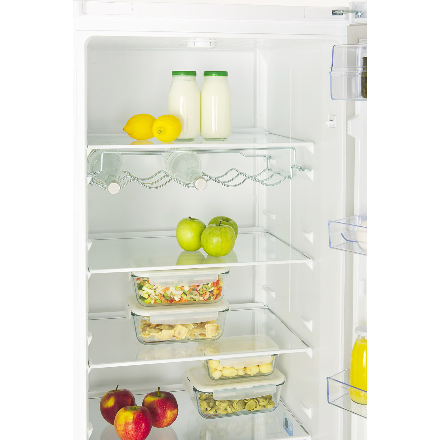 Refrigerator interior with fruits, vegetables, milk bottles, and glass containers. Apples, lemons, and green apples are visible.
