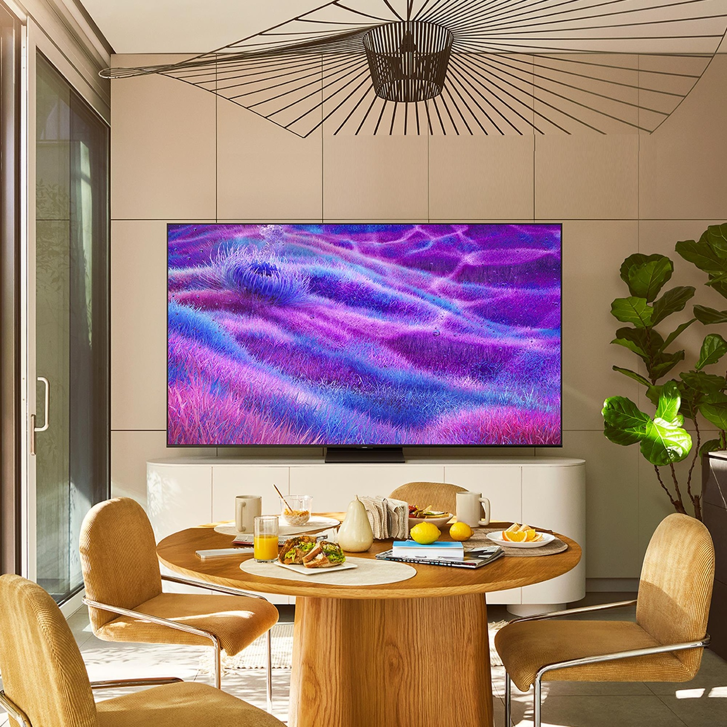 Ambientazione con TV Samsung, tavolo rotondo con cibo, due sedie e pianta.