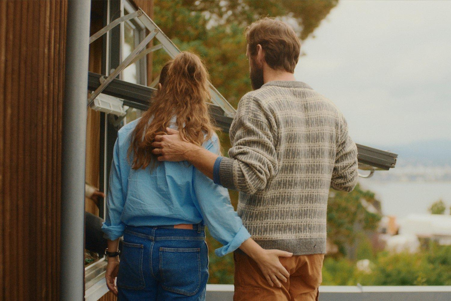 Ein Mann berührt den Hintern einer Frau. Sie stehen an einem Fenster mit Blick aufs Wasser.