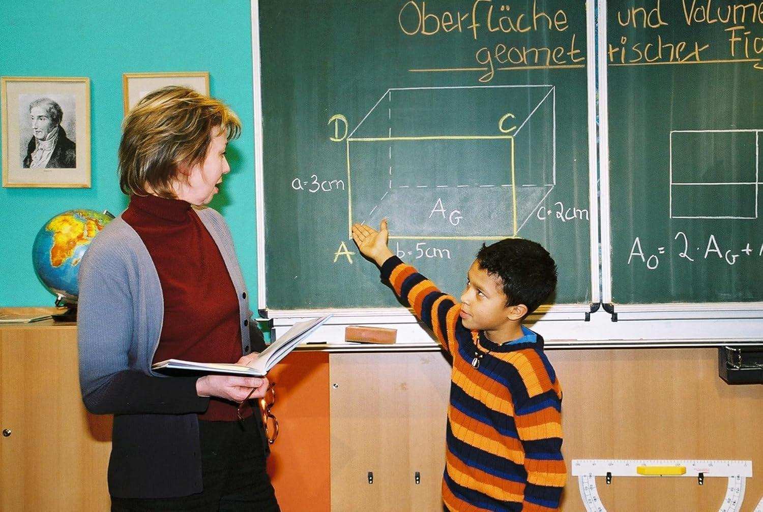 Ein Lehrer und ein Schüler vor einer Tafel mit Geometrie. Andere Schüler sind anwesend.