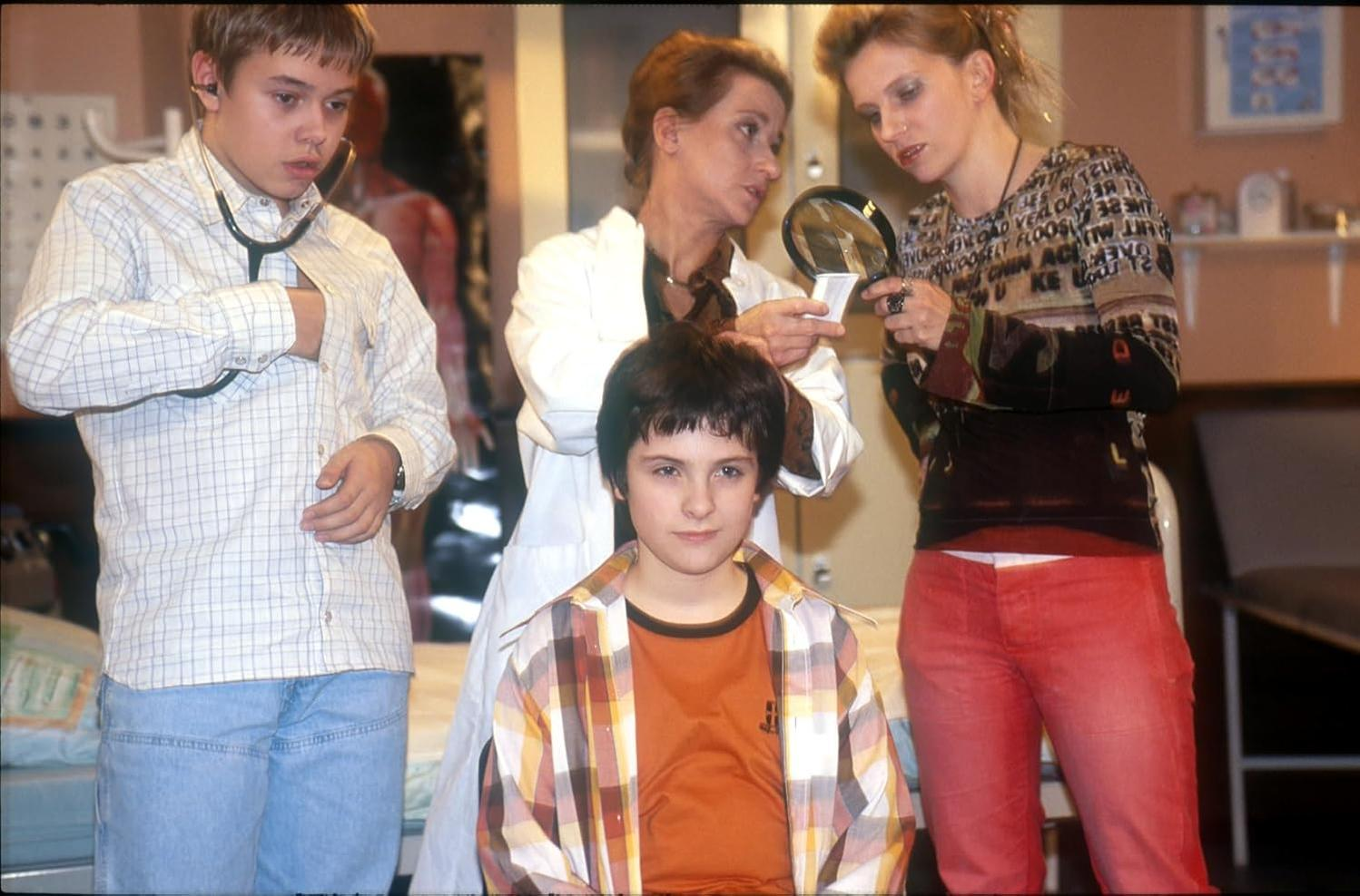 Zwei Ärzte und zwei Kinder in einem Raum. Ein Kind wird mit einer Lupe untersucht.