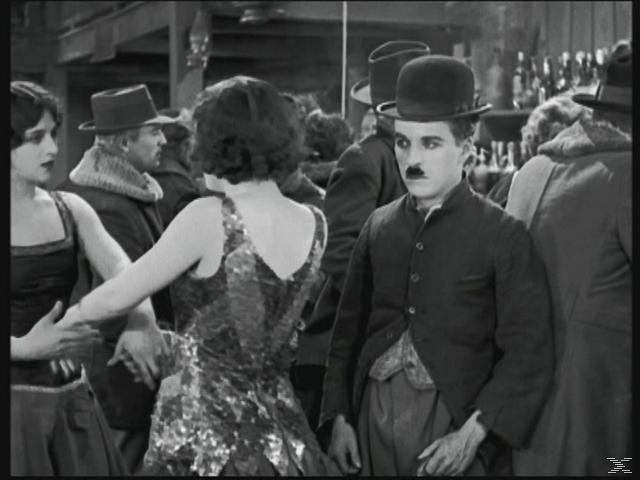 Chaplin in einer Menschenmenge. Schwarzweiß, Stummfilmära. Chaplin hat einen Schnurrbart.