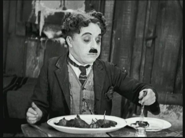 Charlie Chaplin in seiner Rolle, isst von einem Teller. Schwarz-Weiß-Bild.