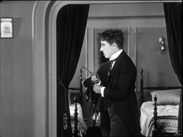 Chaplin im Anzug, der in einer Tür steht und etwas außerhalb der Kamera betrachtet. Schwarzweiß.