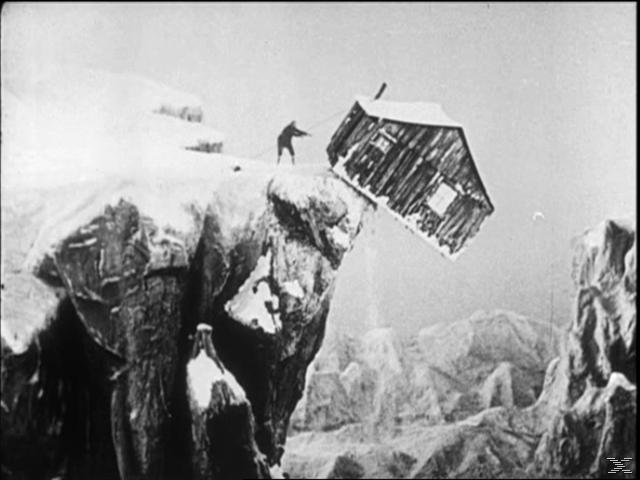 Haus auf einer Klippe wird weggestoßen. Figur, die es schiebt. Eis und Schnee, schwarz und weiß.
