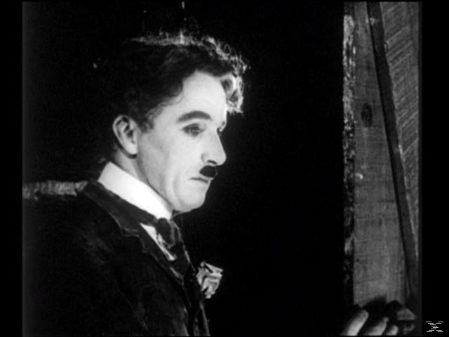 Chaplin in einem Türrahmen, der zur Seite blickt, ernster Ausdruck. Schwarz und Weiß.