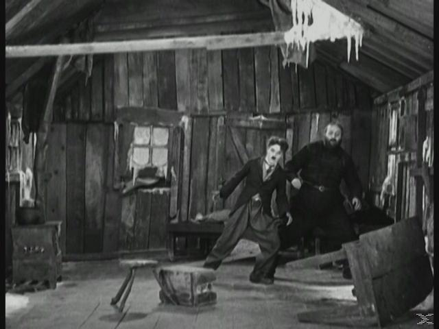 Chaplin und ein anderer Mann in einer Hütte, Chaplin fällt. Schwarz und Weiß.