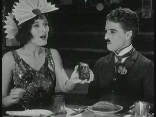 Ein Mann und eine Frau sitzen an einem Tisch. Sie halten ein Foto. Ein Glas und Brot auf dem Tisch.