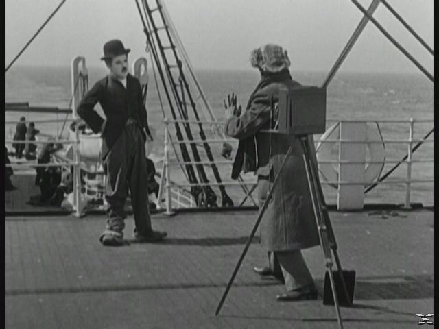 Mann mit Hut und Mantel, ein anderer macht ein Foto auf einem Schiffsdeck.