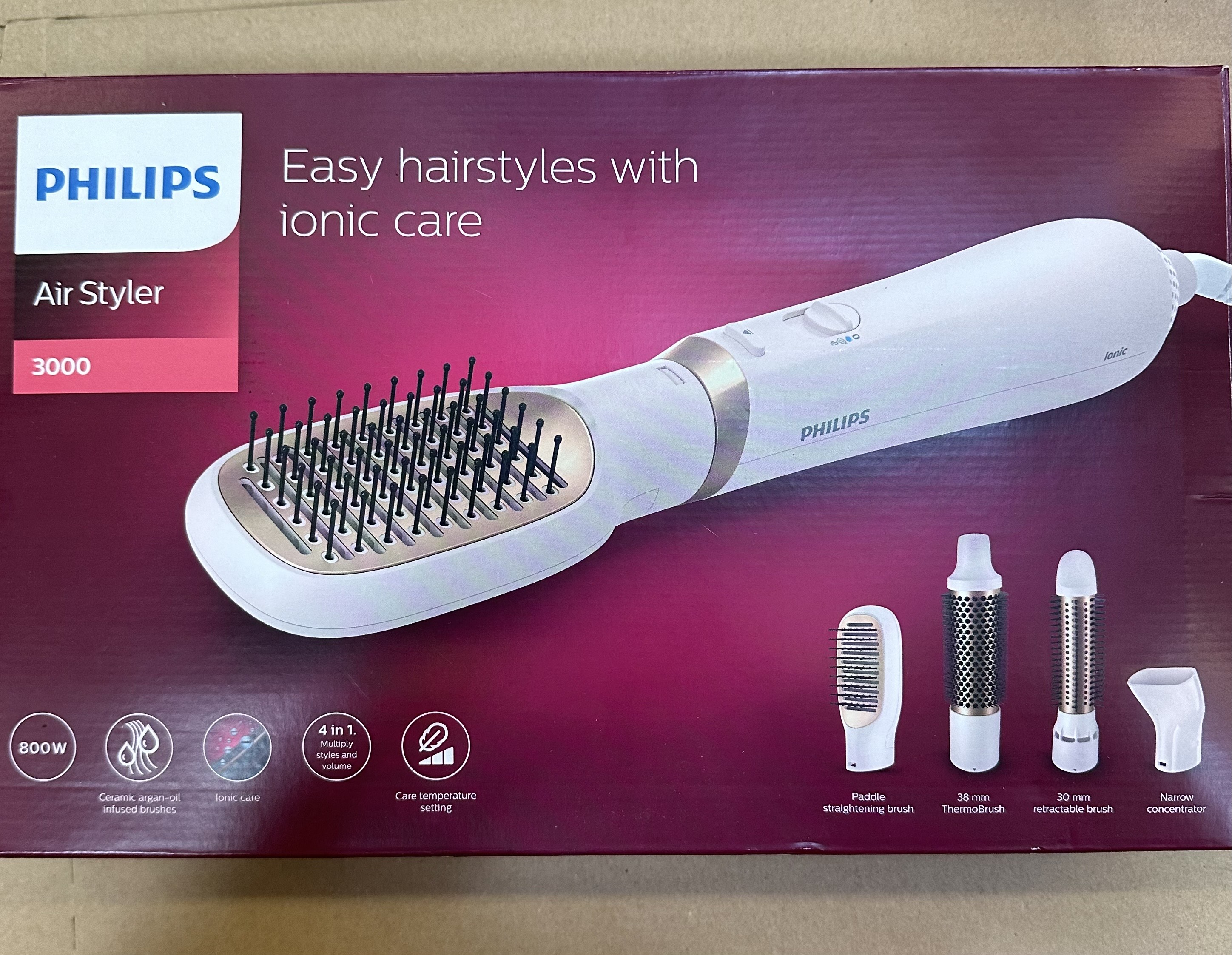 Philips Air Styler w pudełku. Biało-złoty design. Zawiera akcesoria. Bordowe tło.