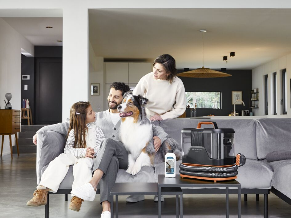 Familia con perro en el sofá. Aspiradora en la mesa. Salón moderno. La gente mira al perro.