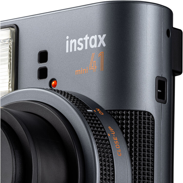 Egy szürke instax mini 41 instant fényképezőgép közelképe, objektívvel és tárcsával.