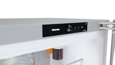 Bir Miele buzdolabının içinde, bir ekran 5°C ve -18°C gösteriyor. Bir kavanoz reçel ve bir cam kap görünür.