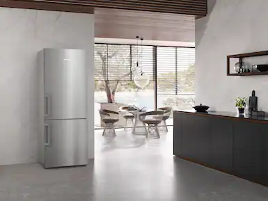 Paslanmaz çelik buzdolabı, masa ve sandalyelerle yemek alanı ve koyu dolaplarla modern mutfak. Parlak, minimalist tasarım.