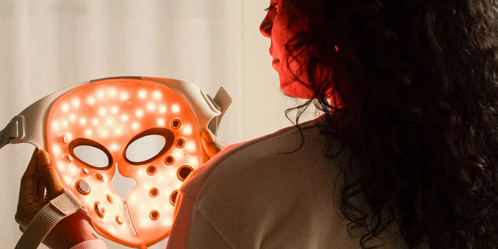 Kobieta trzyma maskę z włączonymi światłami, tyłem do kamery. Maska świeci na czerwono.