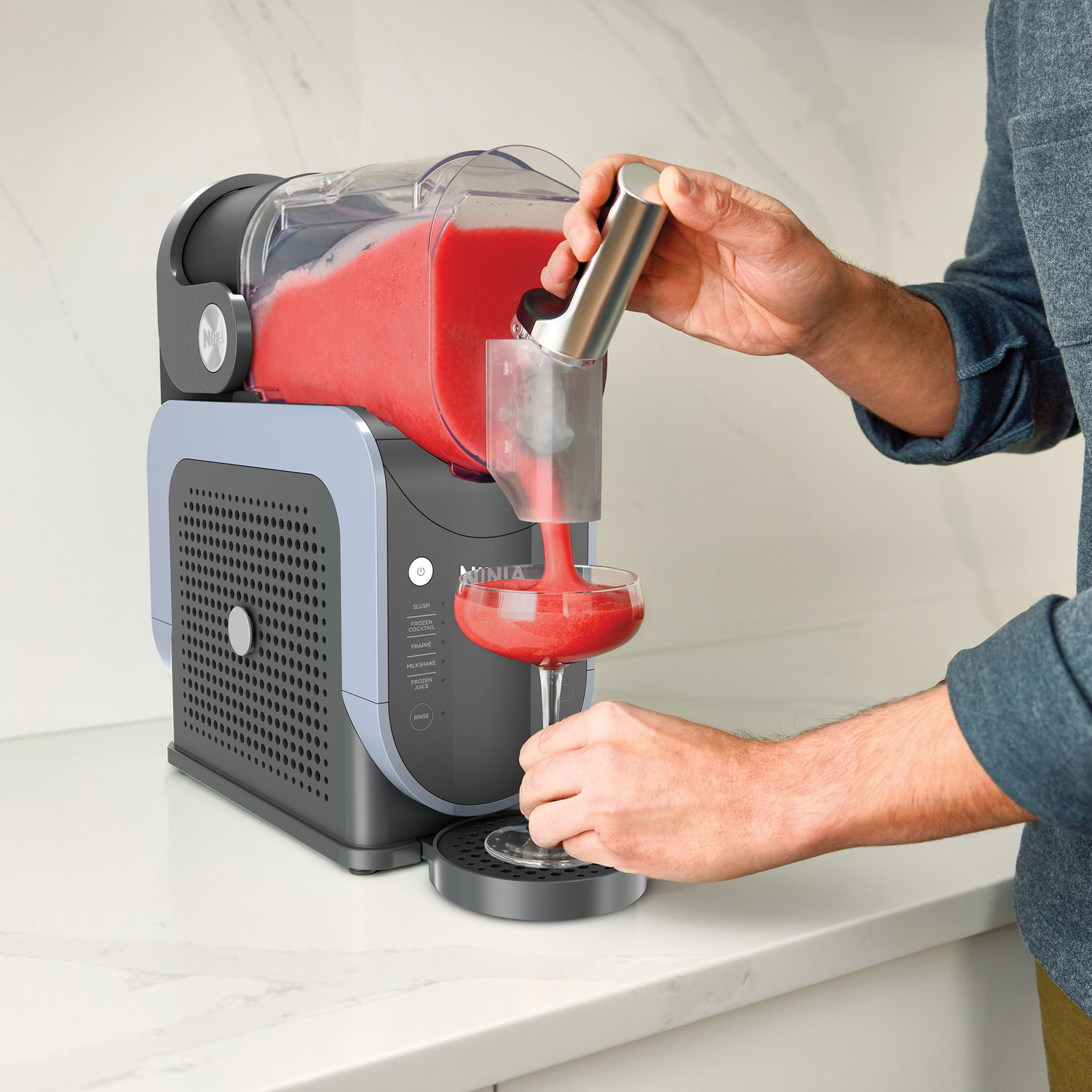 A person pouring red slush from a Ninja machine into a glass.