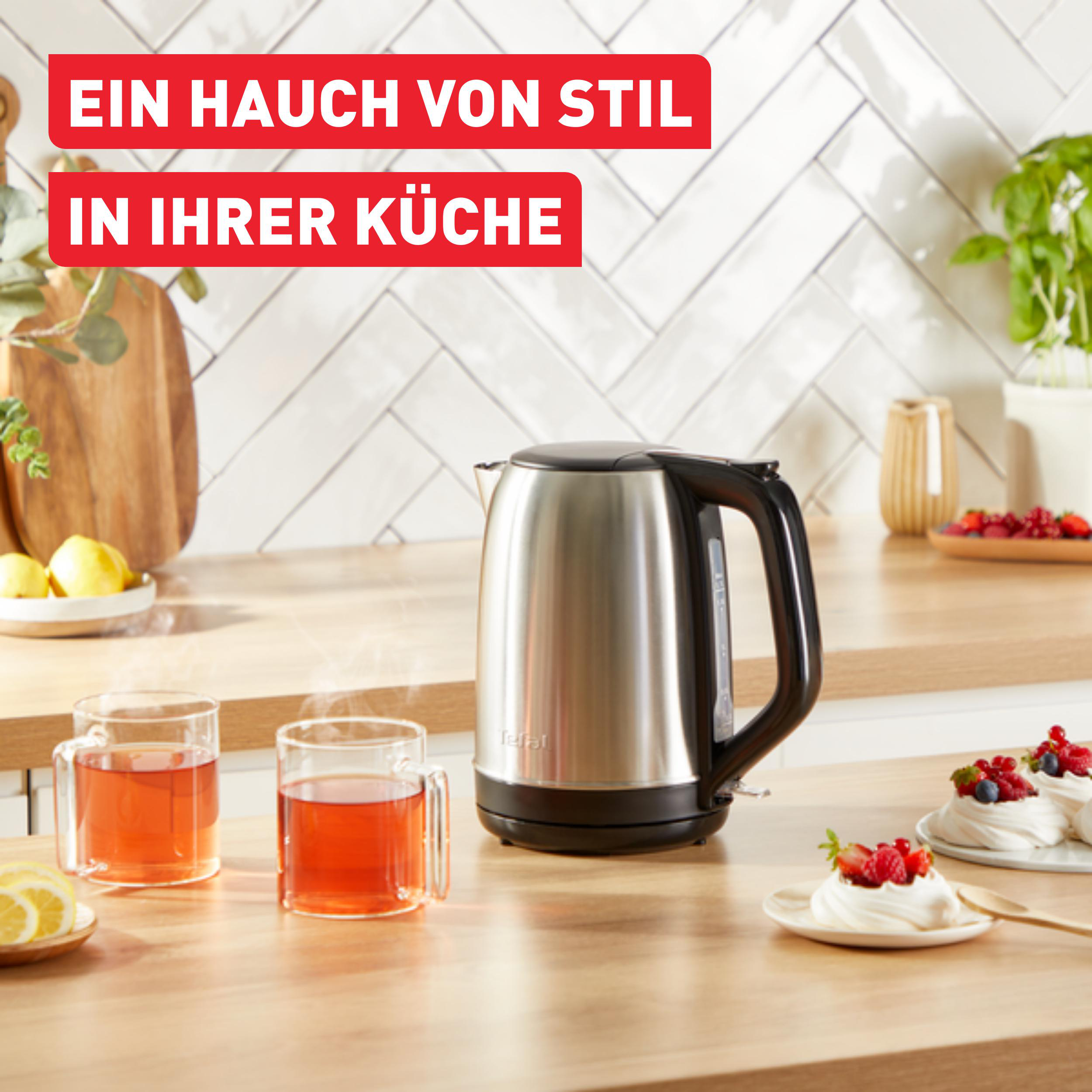 Ein Edelstahl-Tefal-Wasserkocher auf einer Holztheke, mit Tee und Dessert.
