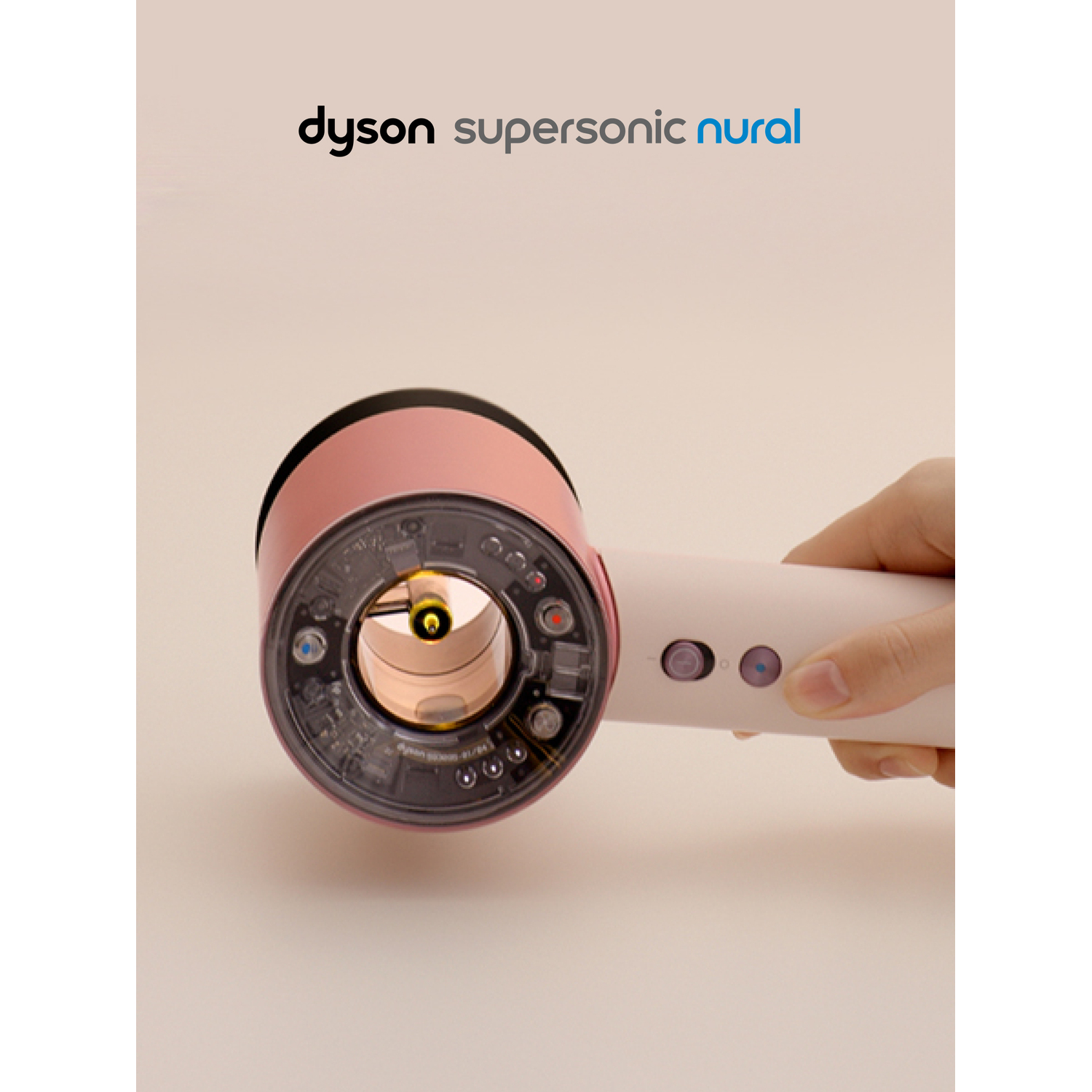 A pink and white Dyson Supersonic Nural hairdryer is held by a hand. The interior components are visible. The background is light.