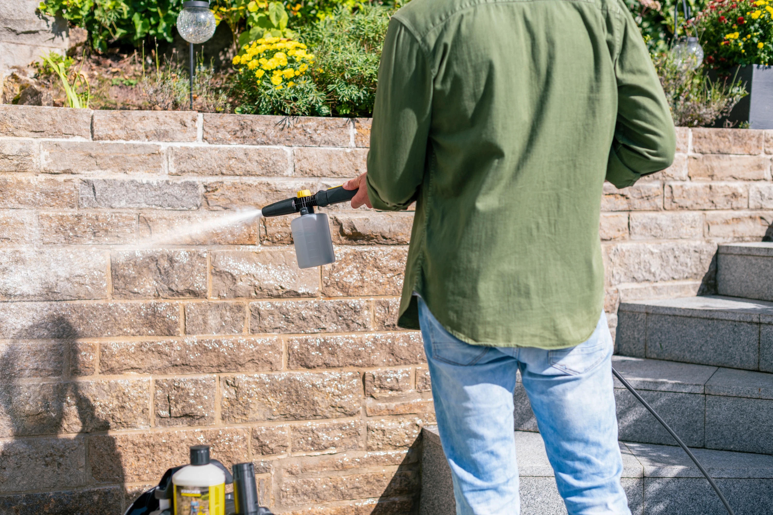 Mężczyzna spryskuje wodą ceglany mur myjką ciśnieniową.
