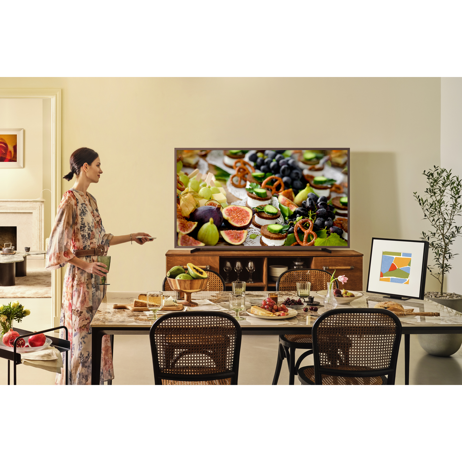 Woman in a room with TV on a buffet. Table set with food.  Woman holding a drink.