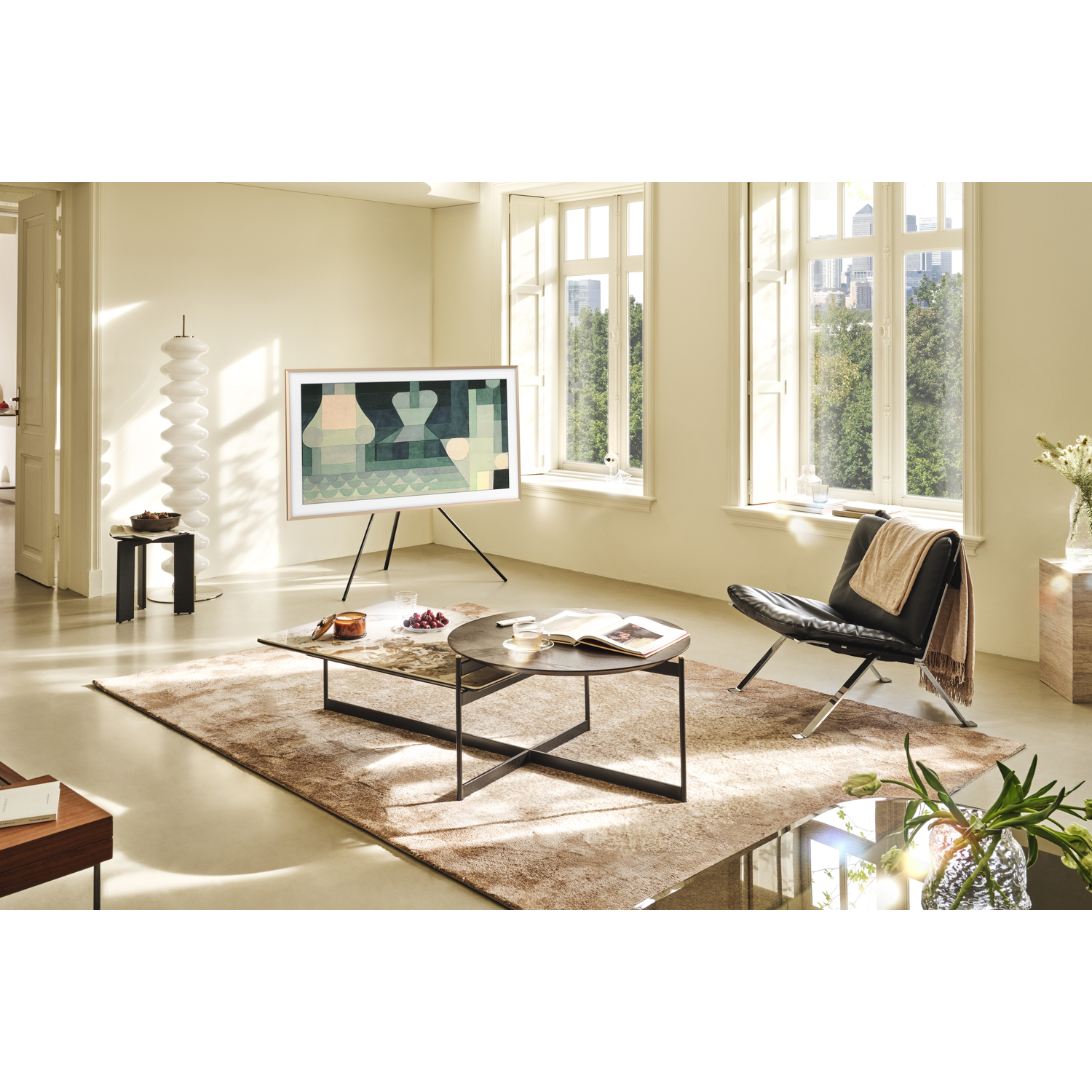 Living room with TV on a tripod, coffee table, rug, chair, and large windows.