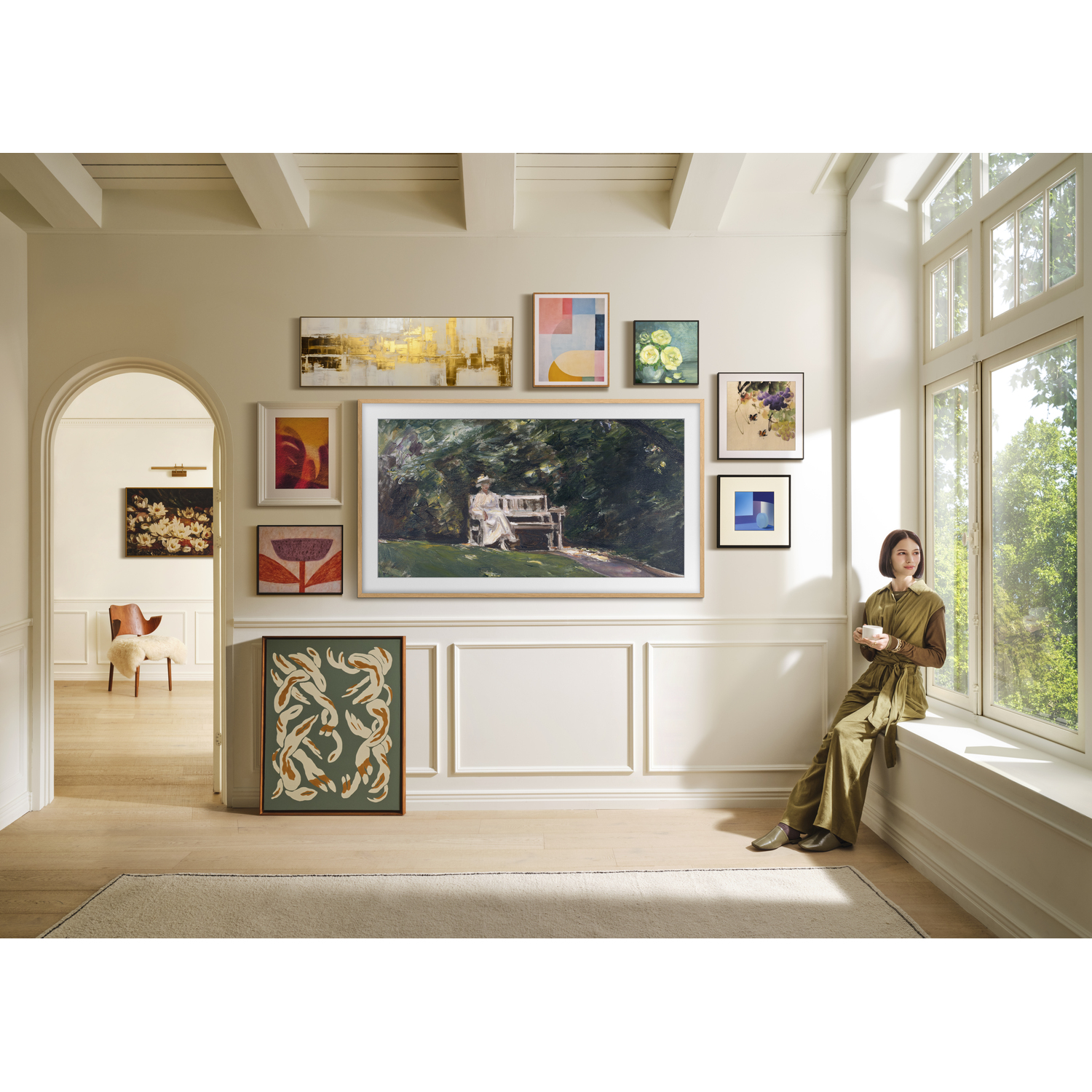 Woman sitting by a window with multiple artworks and a TV on the wall. The room has a classic design.