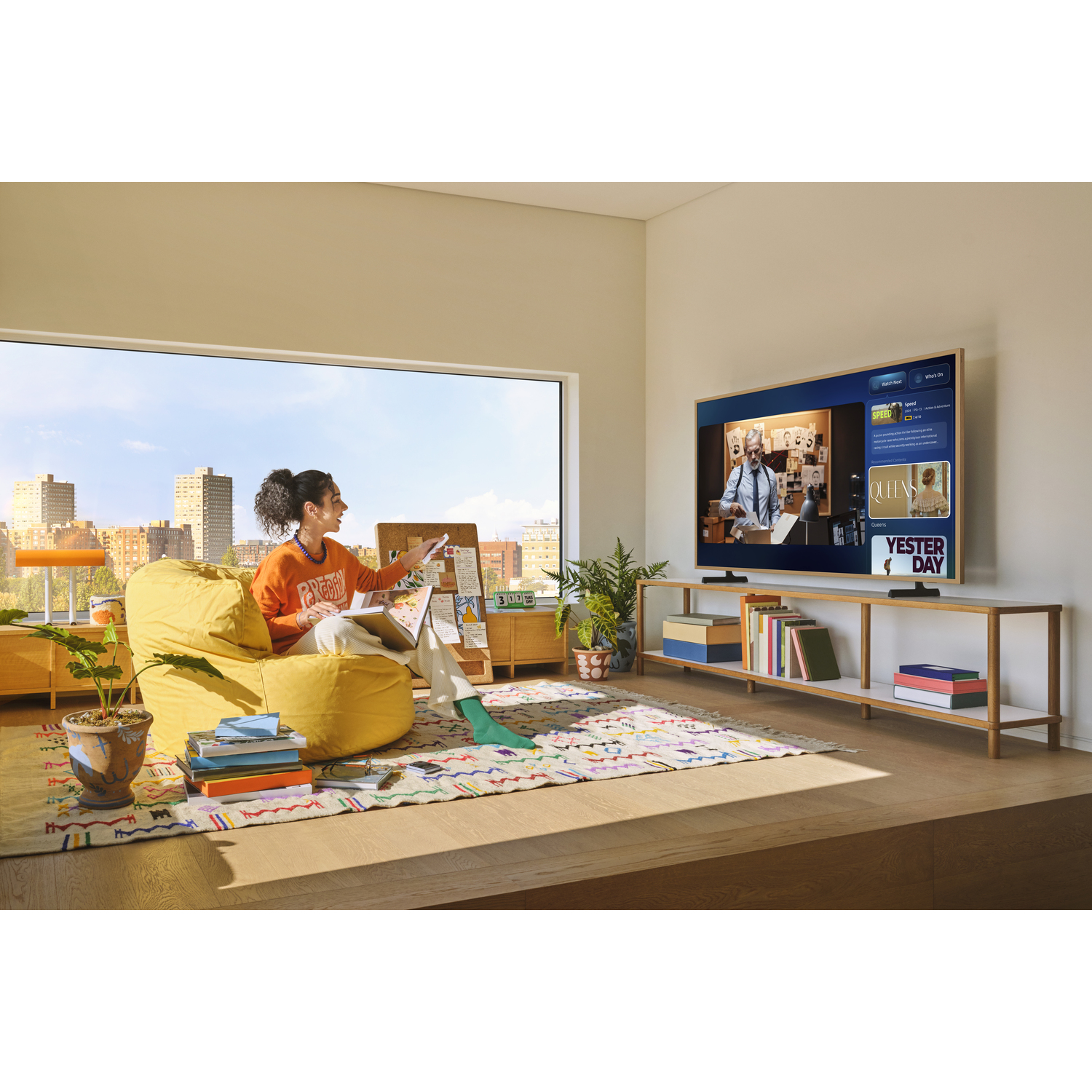 A woman in a living room painting while watching TV. A city is visible through the window.