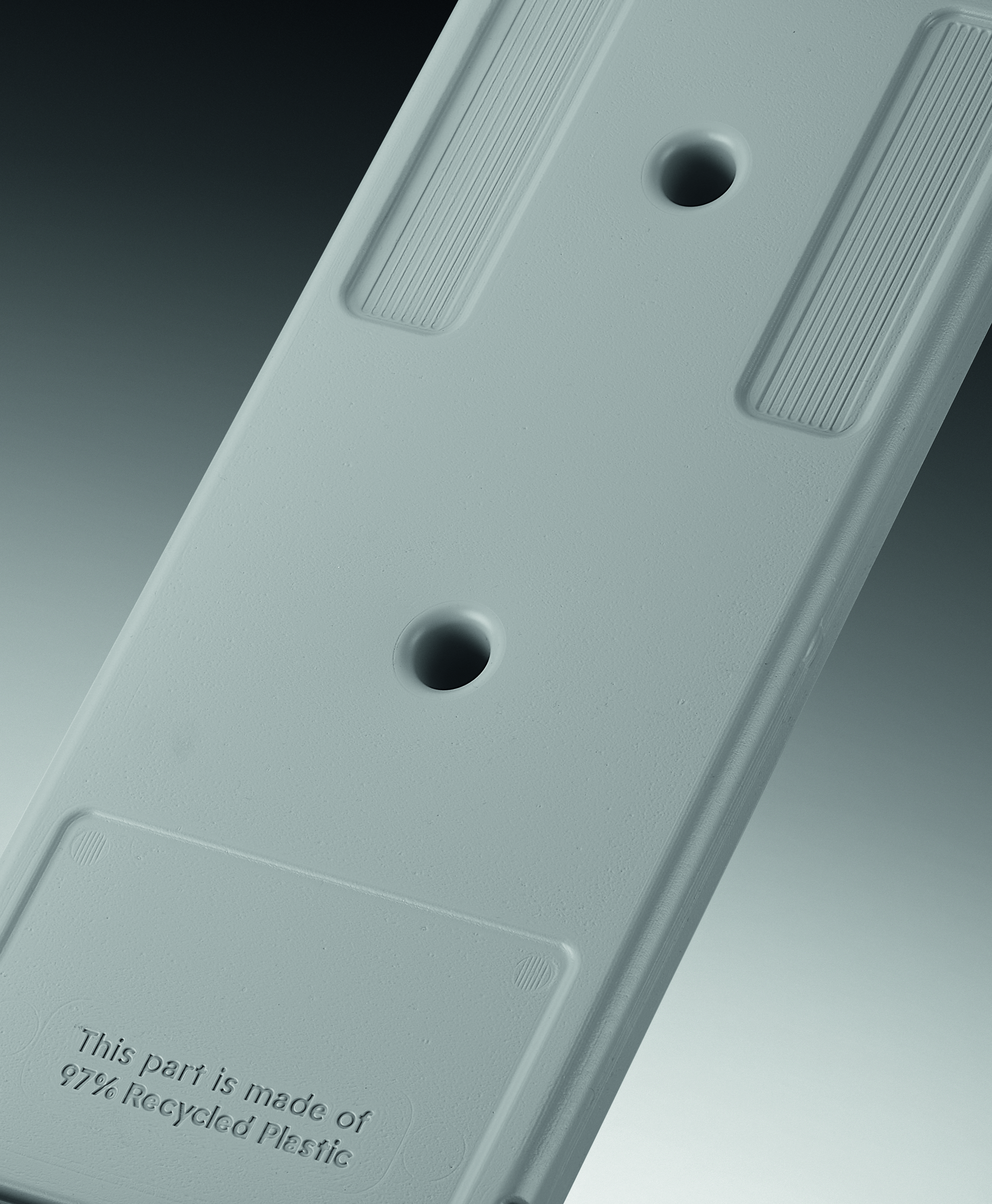 Gros plan sur une pièce en plastique grise. Elle comporte deux trous et le texte 'Cette pièce est fabriquée à partir de 97 % de plastique recyclé'.