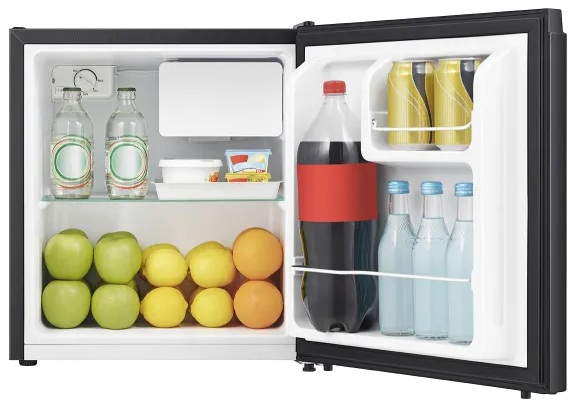 Mini lodówka otwarta, wypełniona owocami, napojami i przyprawami. Zawiera jabłka, pomarańcze, cytryny, butelki wody, sodę i jogurt.