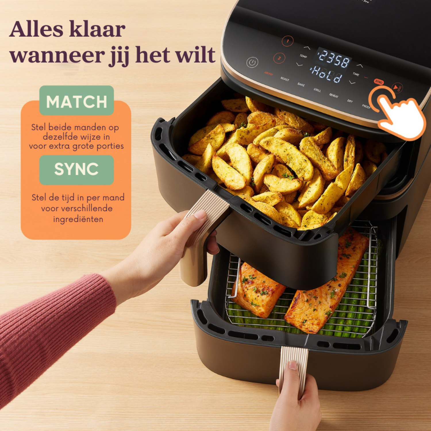 An air fryer. The top basket has potatoes, and the bottom has salmon. A hand is holding the top basket.