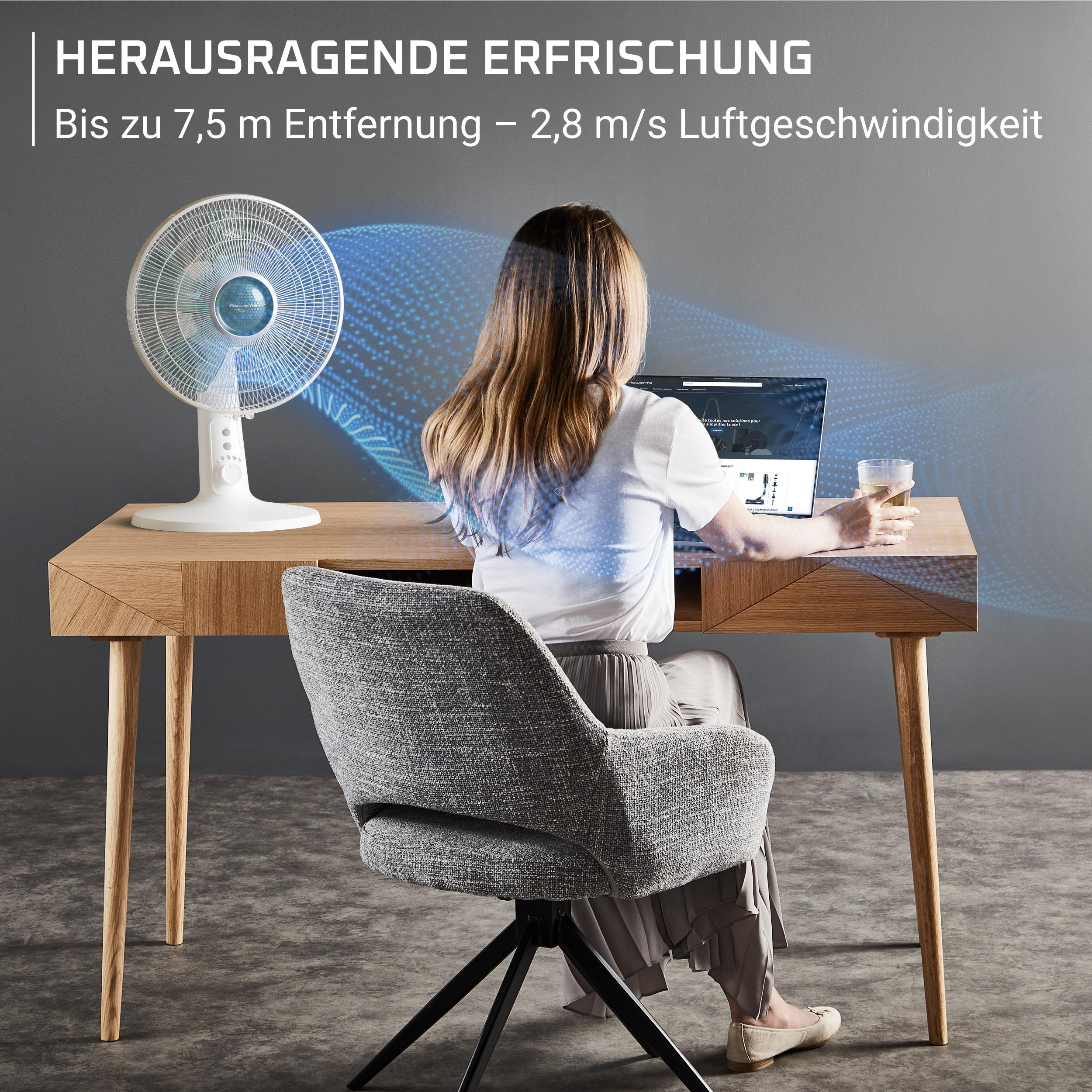 Frau am Schreibtisch, Fan bläst Luft. Laptop, Glas, Stuhl, Tisch.
