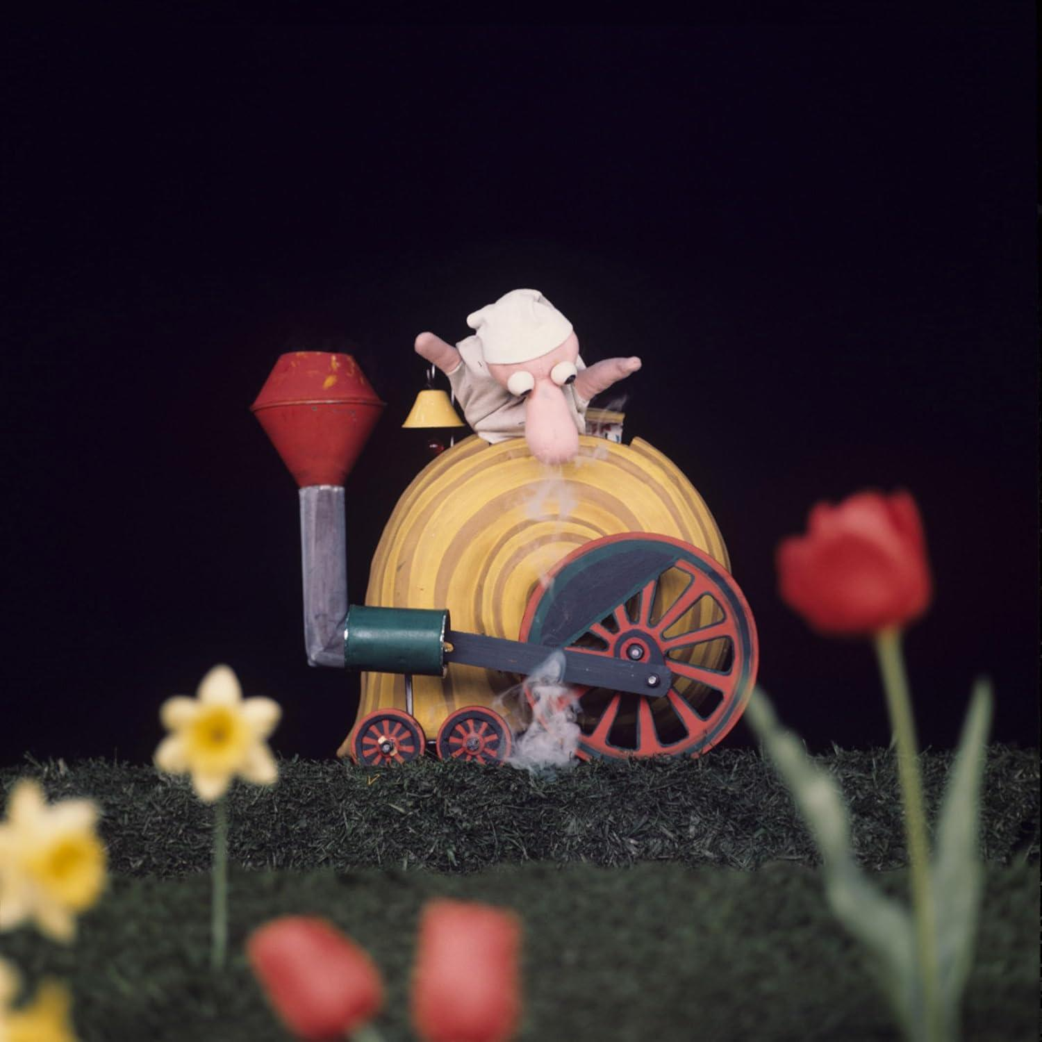 Eine Marionettenbahn mit einer Figur und ein paar Blumen im Vordergrund.